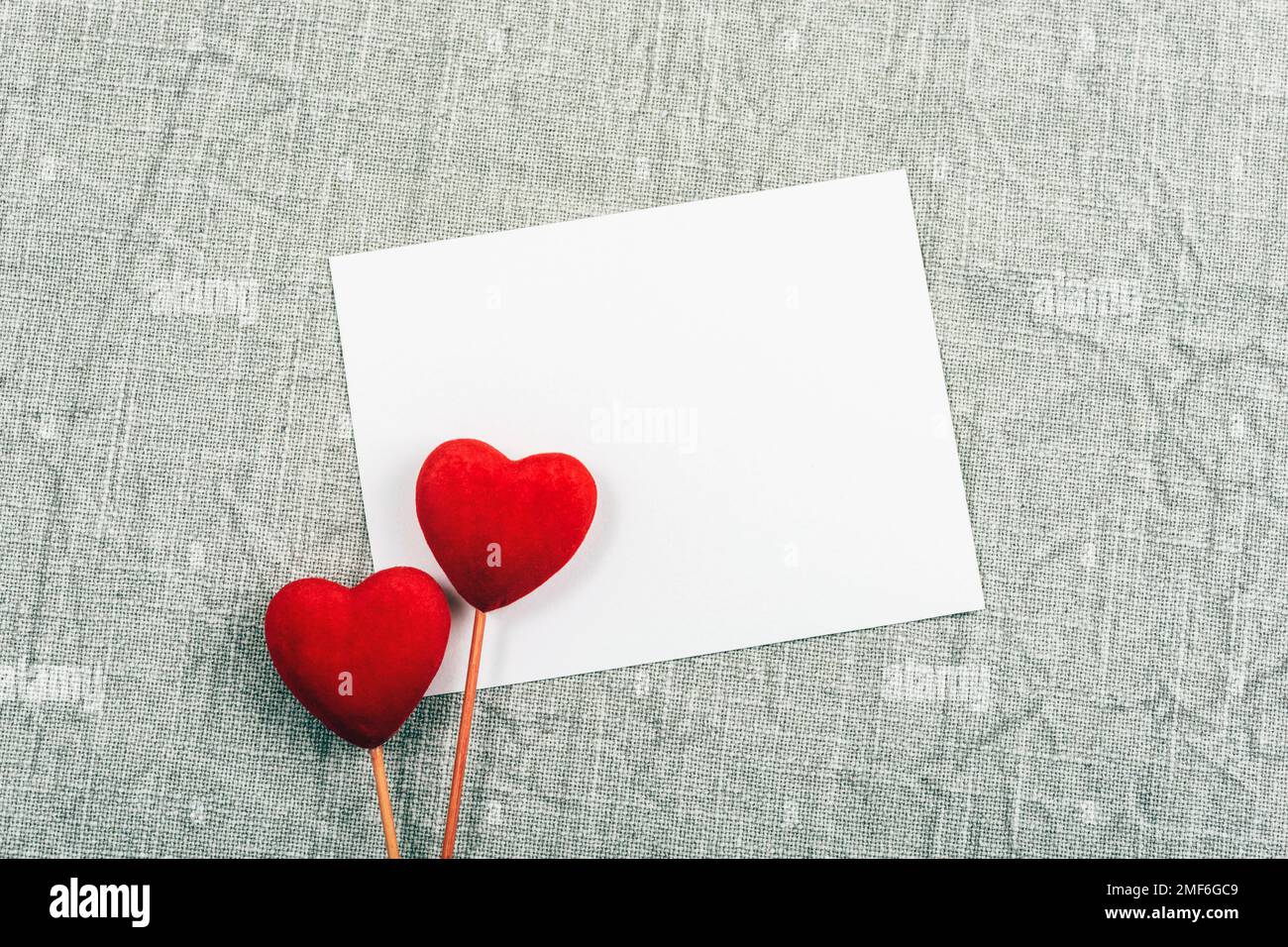 Carte vierge, deux coeurs rouges sur fond textile gris. Concept de la Saint-Valentin. Vue de dessus, plan d'agencement, maquette. Banque D'Images
