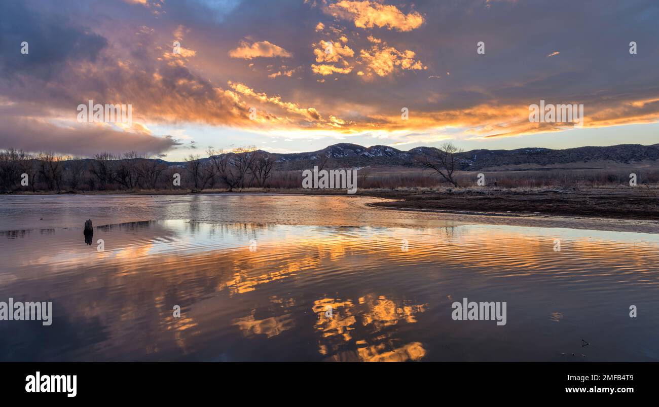 Burning Sky - des nuages colorés au coucher du soleil planant sur une baie à moitié gelée du réservoir de Chatfield lors d'une soirée d'hiver calme. Parc régional de Chatfield, Colorado, États-Unis. Banque D'Images