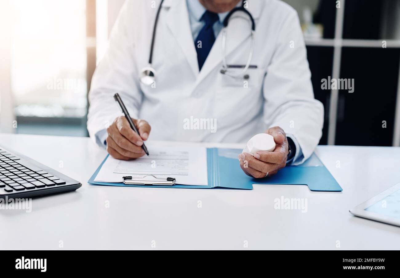 Noter tous les traitements prescrits. un médecin masculin méconnaissable écrit sur un formulaire tout en tenant des médicaments dans son bureau. Banque D'Images