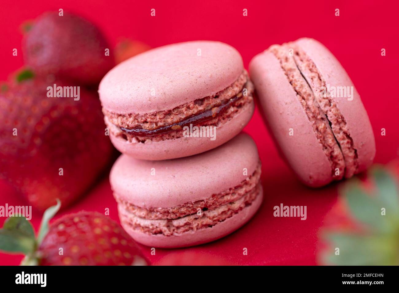 Gros plan studio de paysages de délicieux biscuits de macaron français colorés sur fond rouge avec des fraises. Banque D'Images