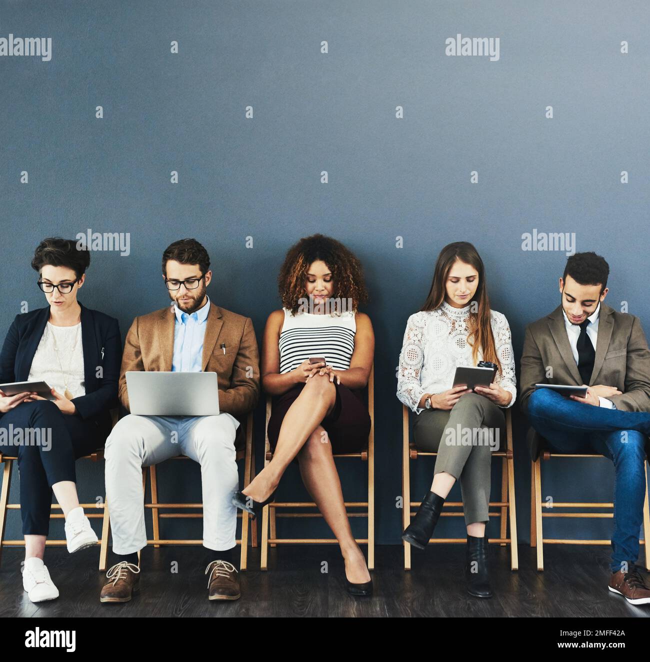 Le processus d'embauche a commencé. Photo en studio d'un groupe d'hommes d'affaires utilisant la technologie sans fil en attendant dans la file d'attente sur fond gris. Banque D'Images