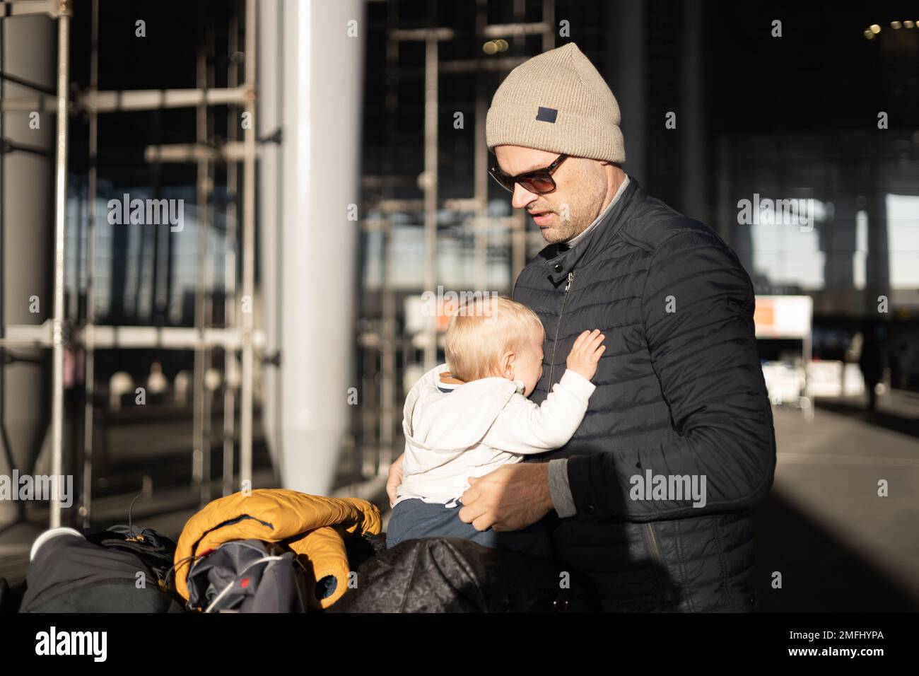 Fatherat réconfortant son bébé en pleurs bébé garçon enfant fatigué assis sur le dessus du chariot à bagages devant la gare de l'aéroport tout en voyageant avec la famille Banque D'Images