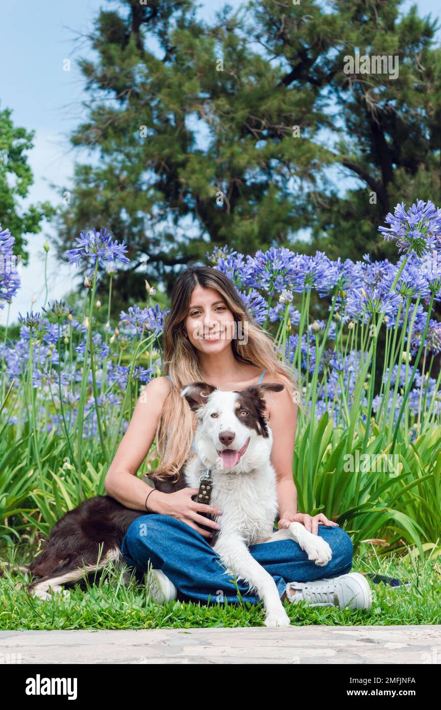 portrait de la jeune femme latina d'origine colombienne, avec de longs cheveux bouclés en bleu, assis dans le parc avec son chien de race collie frontière, souriant et Banque D'Images