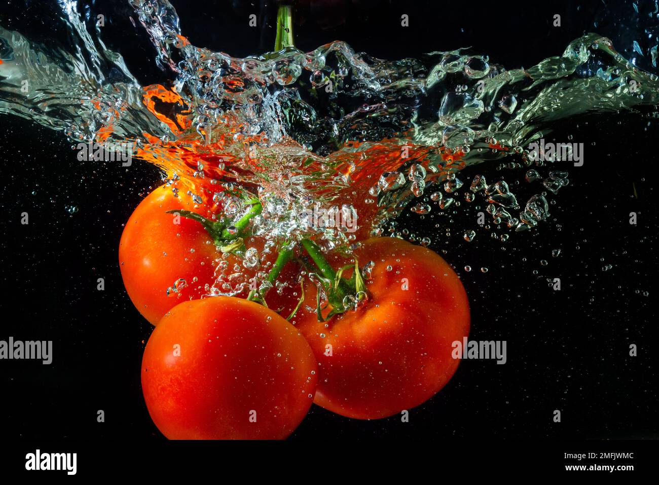 Tomate rouge fraîche tombant dans l'eau avec des éclaboussures d'eau et des bulles d'air isolées sur fond noir. Banque D'Images