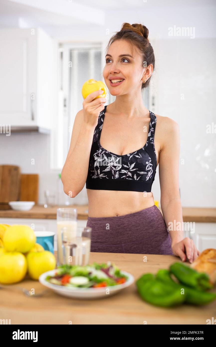 Petite fille sportive mangeant des pommes dans la cuisine pendant le petit-déjeuner Banque D'Images
