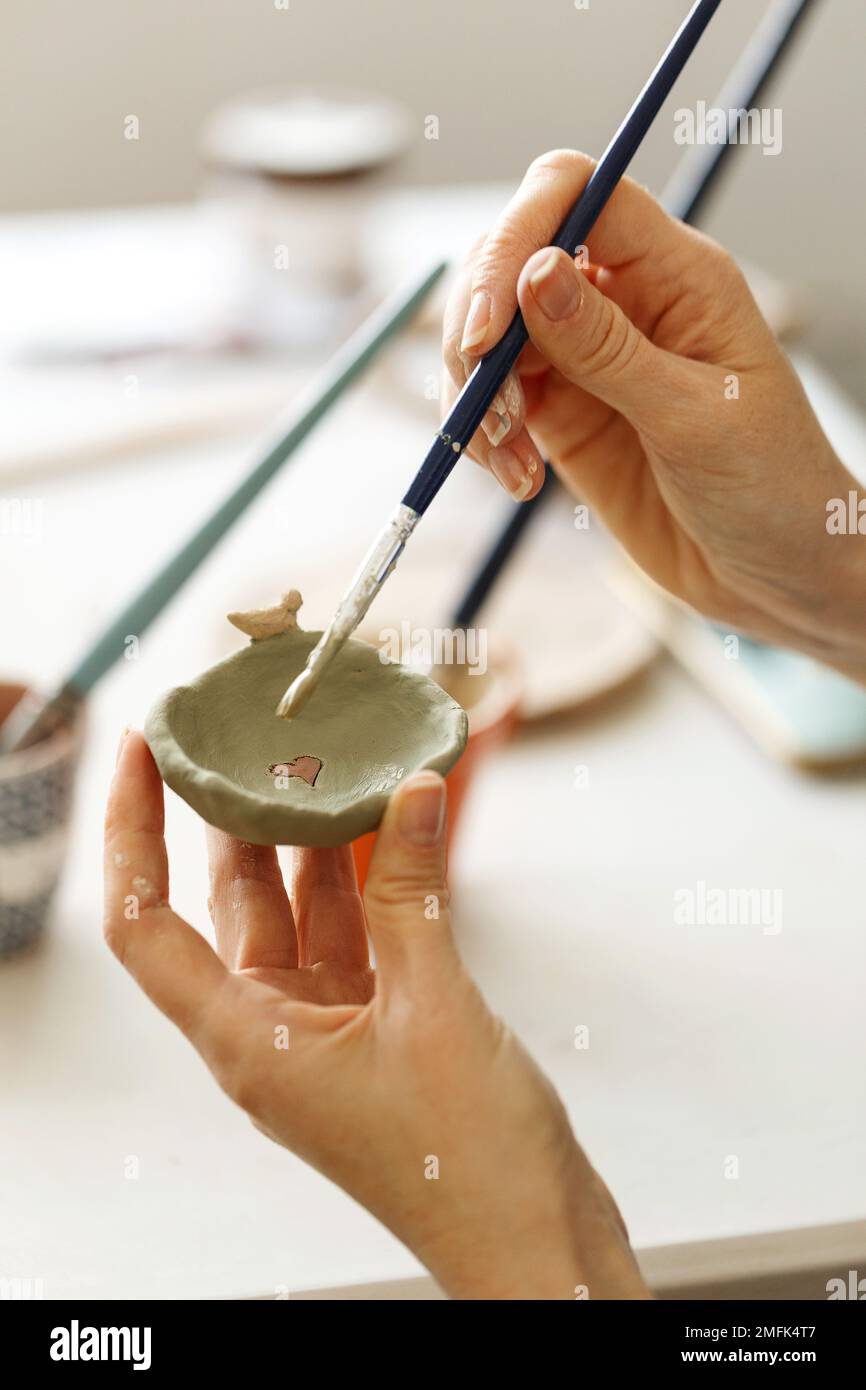 Femme concentrée peignant la carafe d'argile avec la peinture colorée façonnant et sculptant la coupe de faïence dans le studio de poterie sur l'atelier de céramique. Artiste fille r Banque D'Images