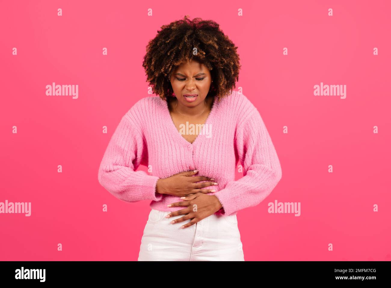 Triste jolie jeune femme noire curly dans la douleur décontractée de l'estomac, douleur menstruelle Banque D'Images