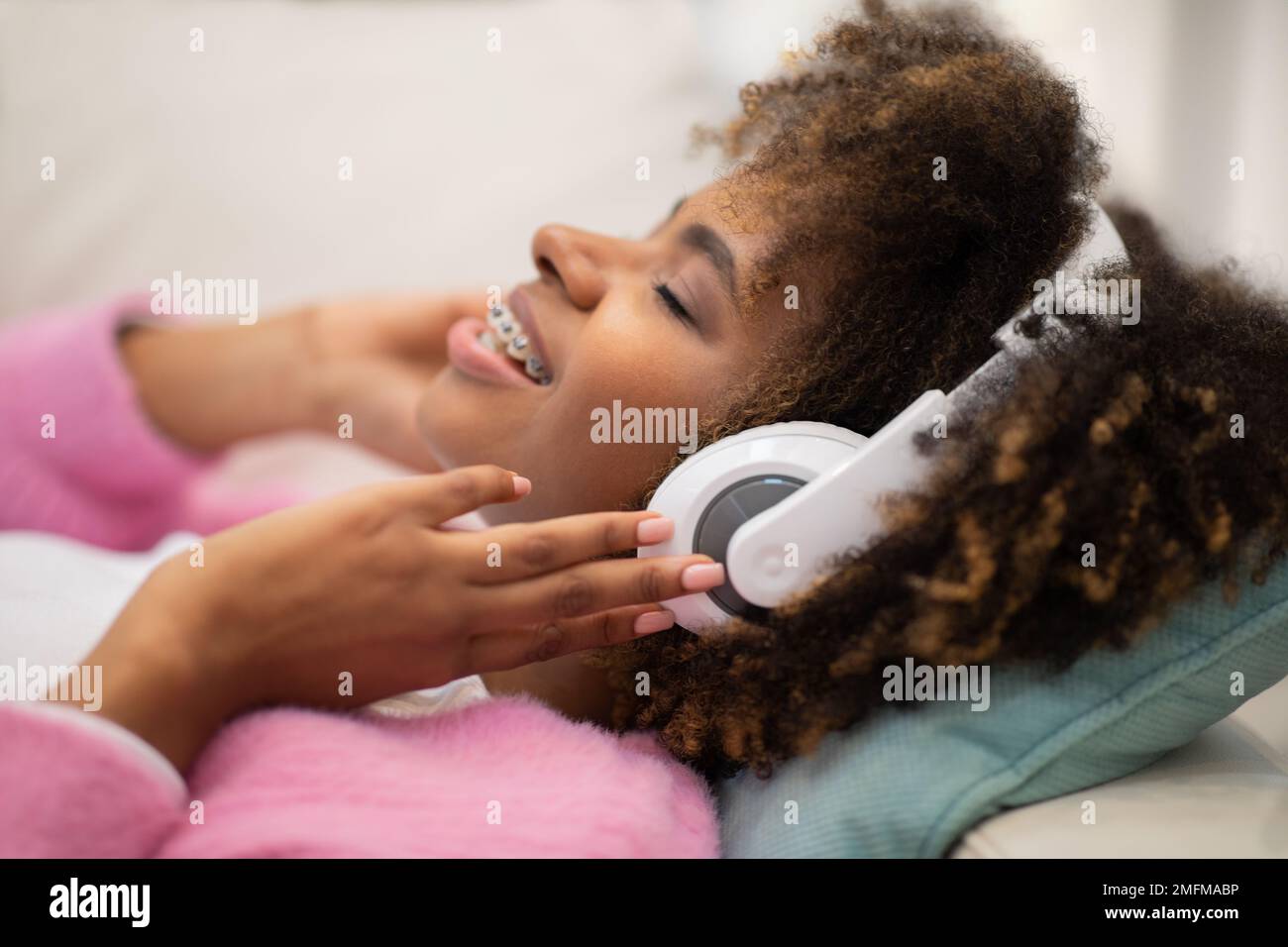 Jeune femme noire joyeuse qui écoute de la musique à l'aide d'un casque sans fil Banque D'Images