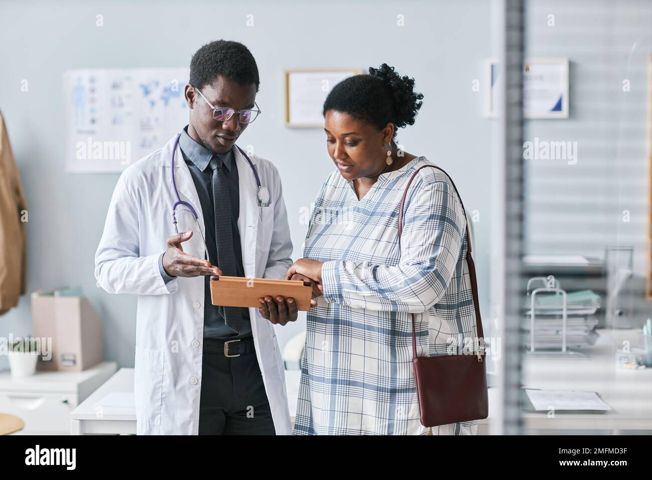 Portrait de jeune médecin noir consultant une patiente et utilisant une tablette numérique en clinique Banque D'Images