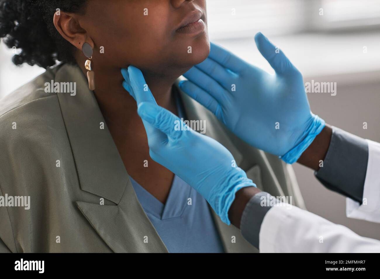 Gros plan d'un médecin masculin méconnaissable qui palpe le cou tout en examinant une femme en clinique Banque D'Images