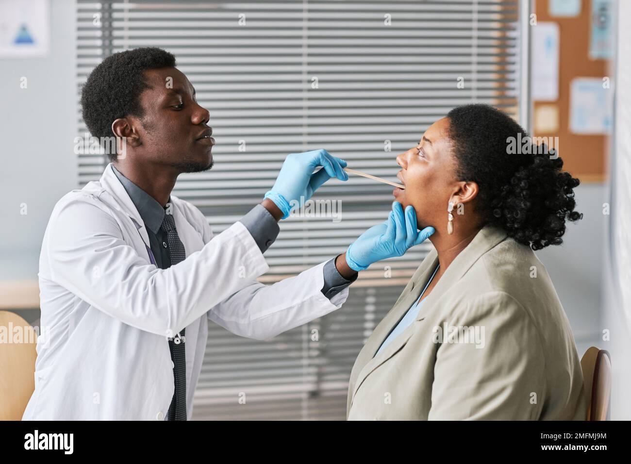 Vue latérale d'un jeune médecin noir examinant une femme en clinique et effectuant un examen de la gorge Banque D'Images