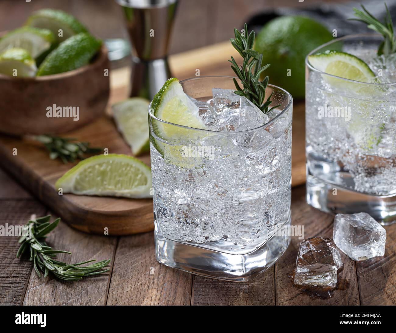 Gin et cocktail tonique avec des tranches de citron vert, du romarin et de la glace sur une table rustique en bois Banque D'Images