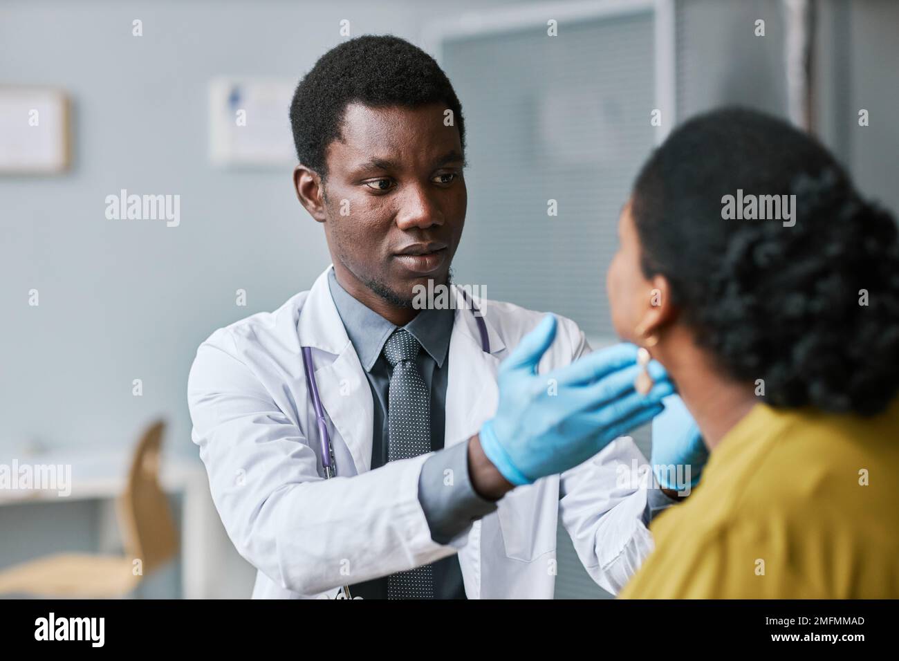 Portrait d'un jeune médecin noir consultant un patient en clinique et effectuant un examen de la gorge avec palpation Banque D'Images