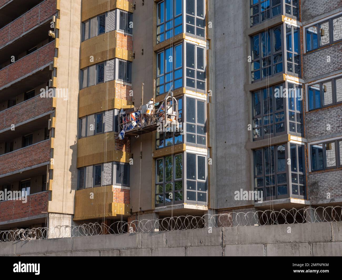 Un constructeur masculin dans un berceau suspendu de construction travaille sur une façade d'une tour nouvellement construite. Nouveau quartier en construction à Kiev. Banque D'Images