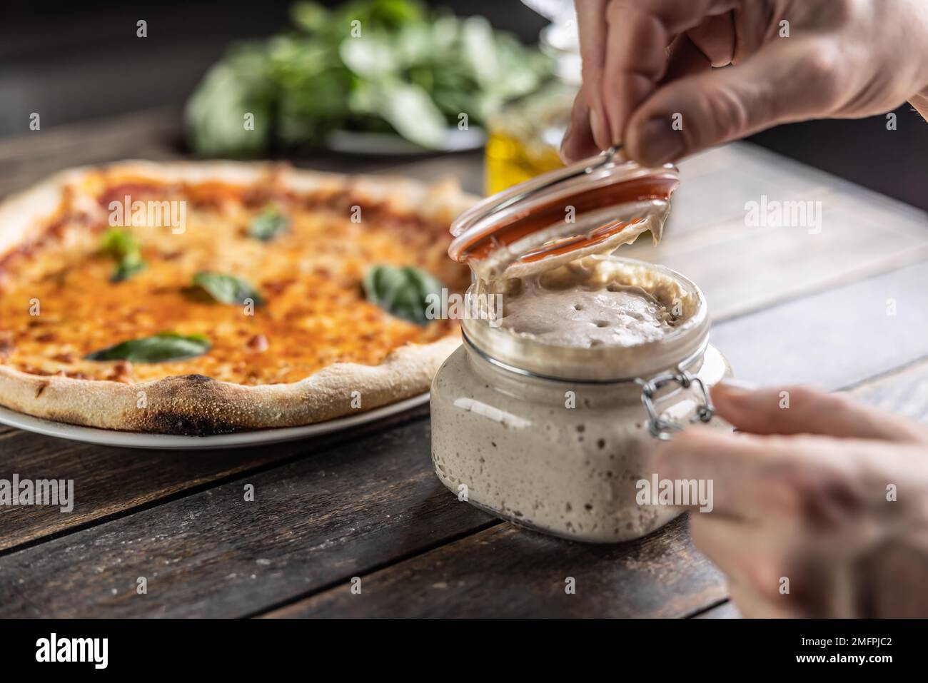 Les mains du cuisinier ouvrent un pot de levain de seigle, en arrière-plan une pizza faite de levain. Banque D'Images