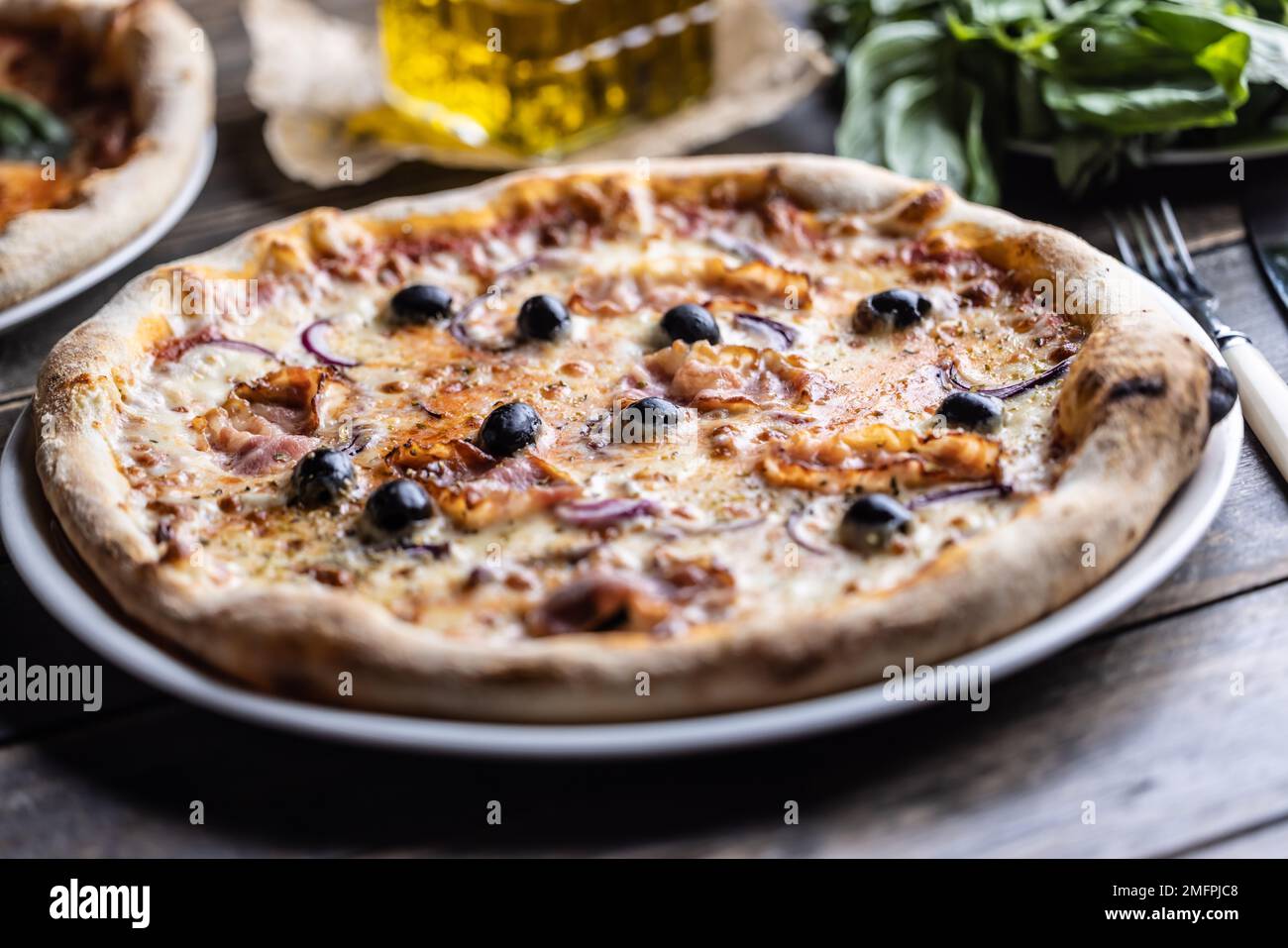 Pizza italienne au bacon avec oignon et olives noires sur une assiette blanche. Banque D'Images