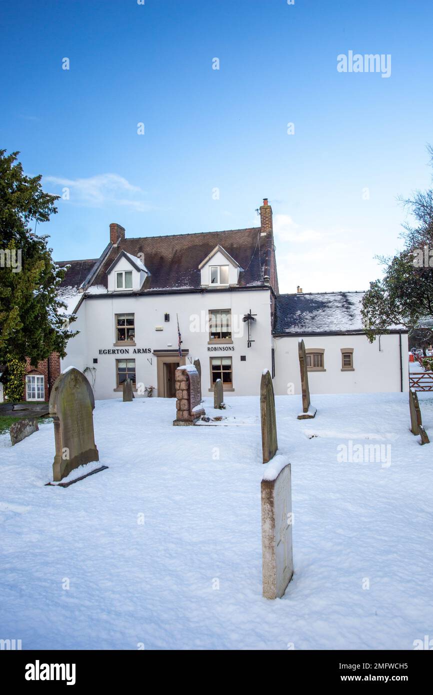Vue de la neige couverte église paroissiale St Mary à Astbury près de Congleton Cheshire Angleterre de la maison publique Egerton Arms en hiver neige Banque D'Images