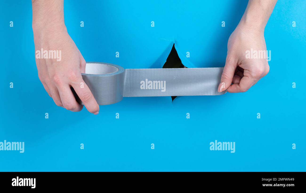 Femme collant de la bande argentée sur un trou sur un fond bleu. Banque D'Images Femme collant de la bande argentée sur un trou sur un fond bleu. Banque D'Images
