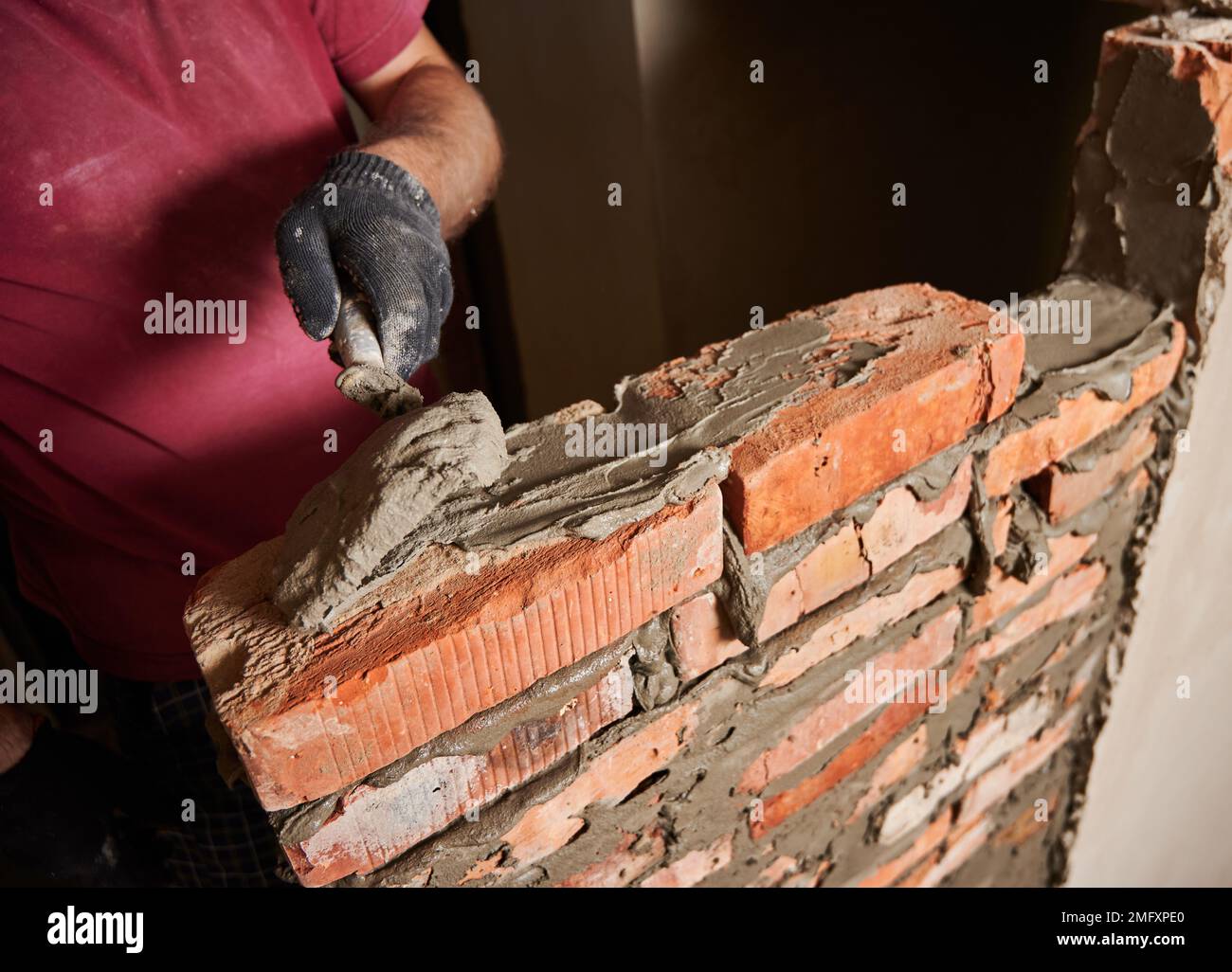 Gros plan de la main mâle dans le gant de travail posant des briques dans le bâtiment en construction. Homme bricklayer constructeur application de mortier de ciment sur les briques avec l'outil de truelle. Concept de construction en maçonnerie. Banque D'Images