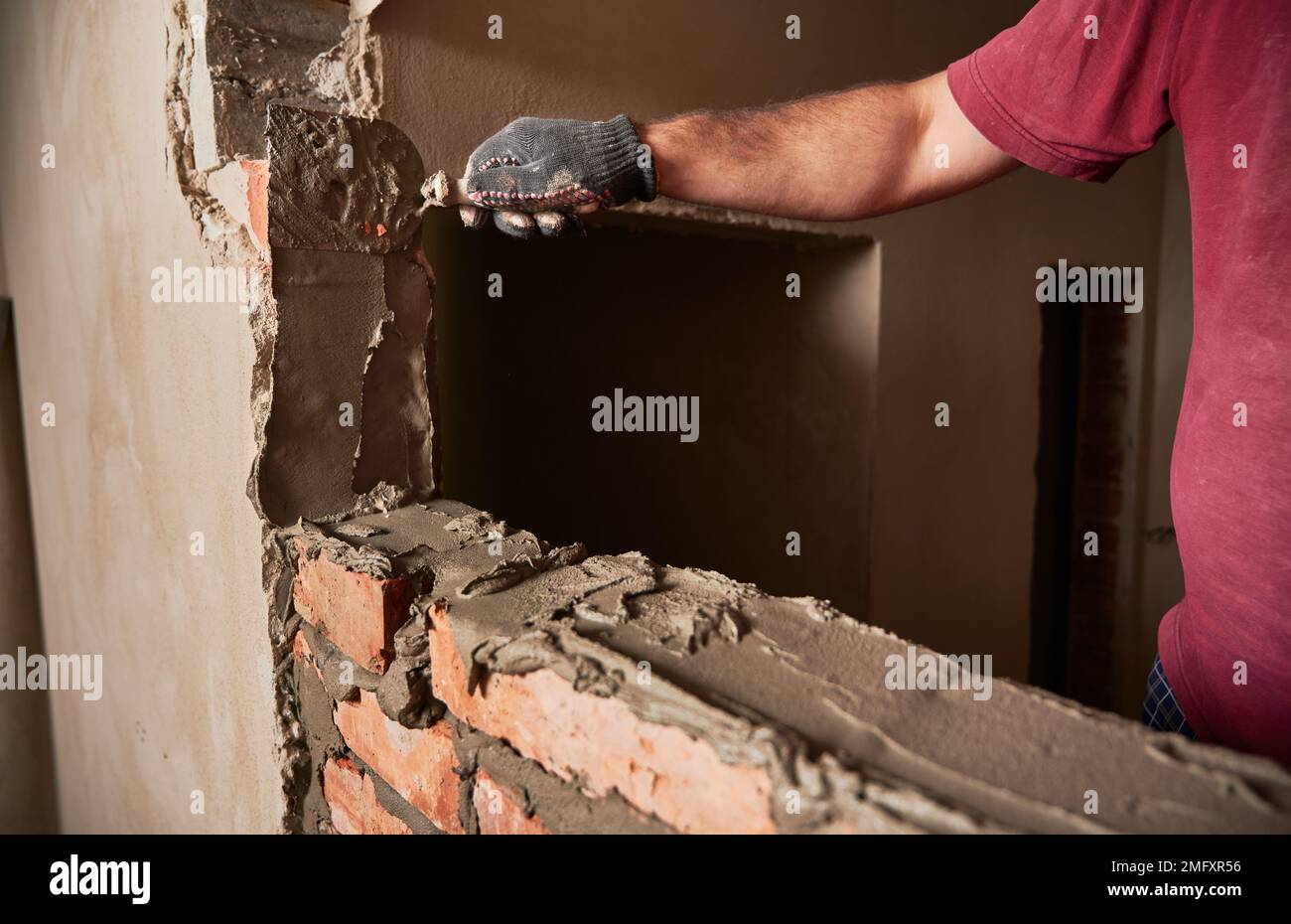 Gros plan de l'homme main dans le gant de travail pose de briques dans le bâtiment en construction. Travailleur masculin appliquant du mortier de ciment sur des briques avec un outil à truelle. Concept de construction en maçonnerie. Banque D'Images