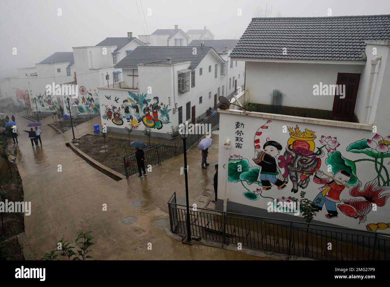 People walk by new village houses decorated with colourful paintings built by the Chinese government for ethnic minority members in Ganluo county, southwest China's Sichuan province on Sept. 10, 2020. The ruling Communist Party says its initiatives have helped to lift millions of people out of poverty. Yi ethnic minority members were moved out of their mountain villages in China’s southwest and into the newly built town in an anti-poverty initiative. (AP Photo/Andy Wong) Banque D'Images