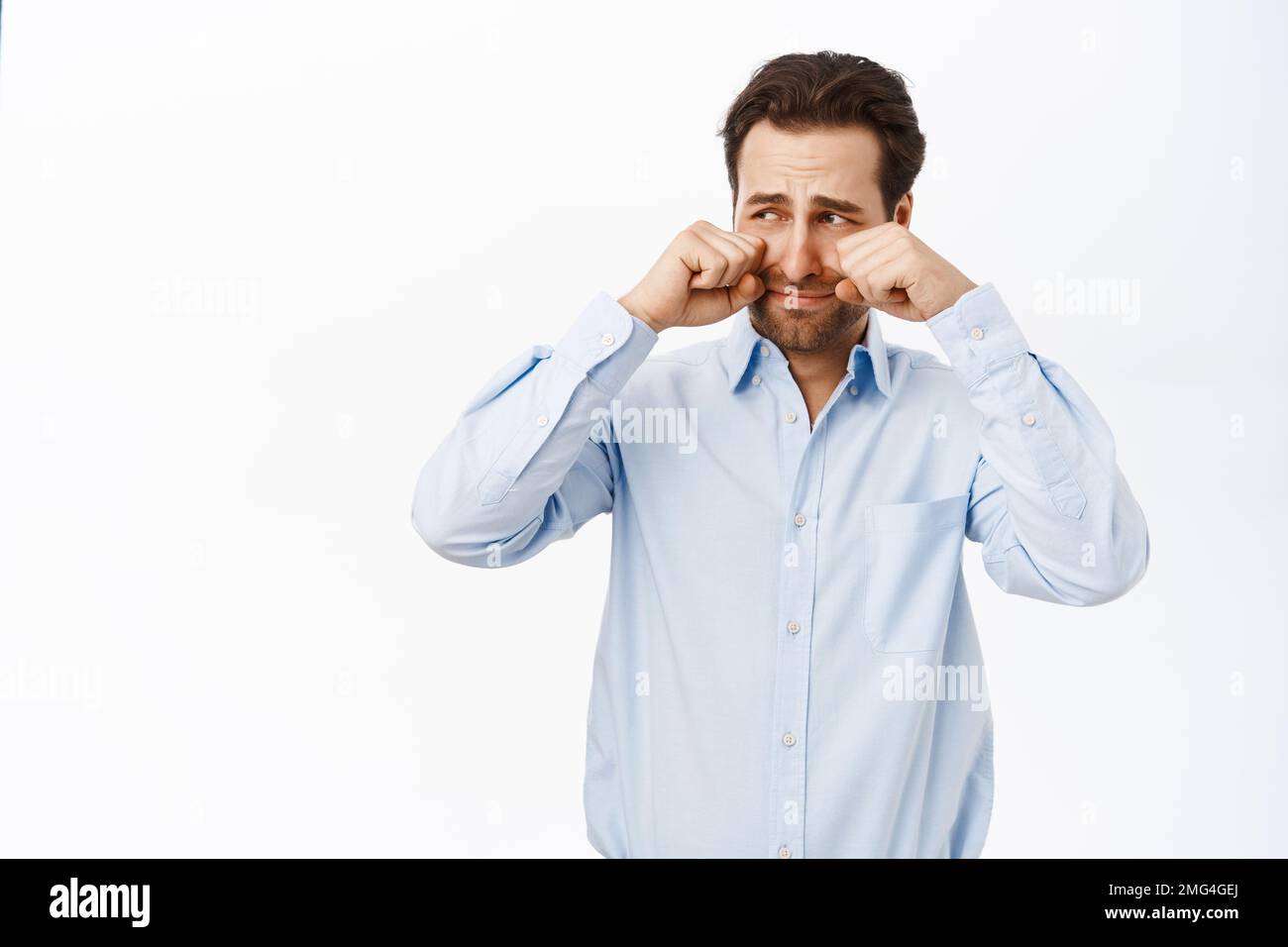 Homme adulte pleurant et essuyant ses larmes, ayant l'air triste ou offensé, en boussant, debout sur fond blanc Banque D'Images