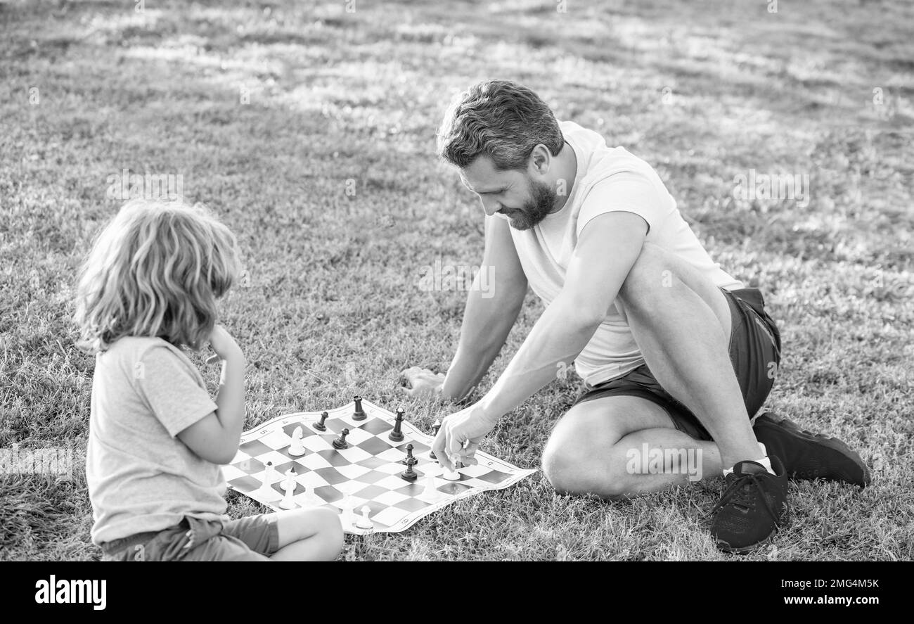 famille heureuse de père homme et son enfant jouant aux échecs sur l'herbe verte dans le parc extérieur, stratégie Banque D'Images
