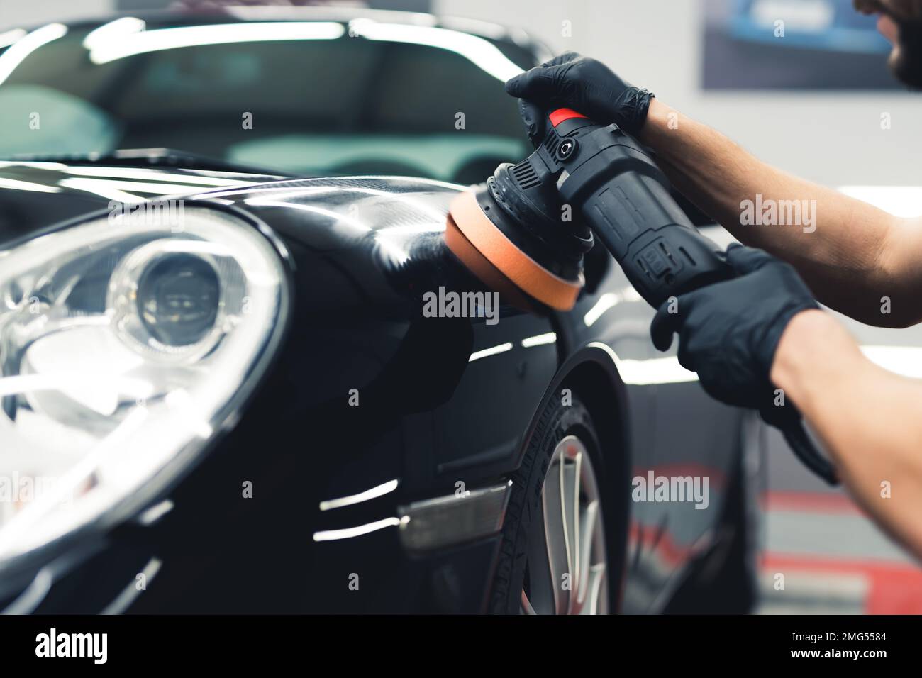 Gros plan d'un homme portant des gants noirs pour polir la peinture à l'avant d'une voiture noire à l'aide d'un outil professionnel. Processus d'habillage des voitures. Prise de vue horizontale en intérieur. Photo de haute qualité Banque D'Images