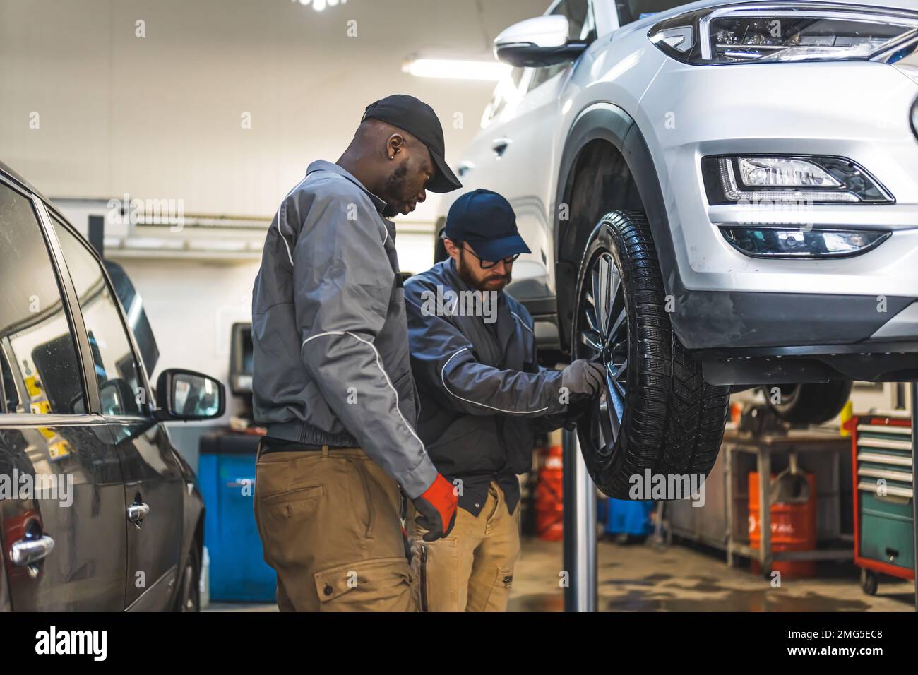 Plan moyen de deux mécaniciens réparant une roue de voiture. Concept atelier de réparation. Photo de haute qualité Banque D'Images