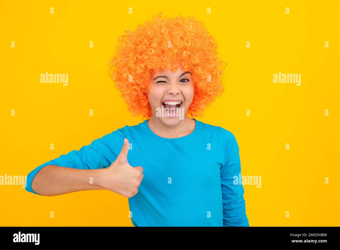 Anniversaire fête d'enfants. Drôle d'enfant dans la perruque clown curly isolé sur fond jaune. Adolescent excité, heureux surpris et surjoyeux émotions. Banque D'Images