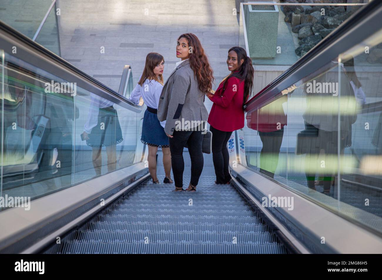 Trois femmes d'affaires sur les escaliers mécaniques dans le bâtiment d'affaires sur leur chemin de travail Banque D'Images
