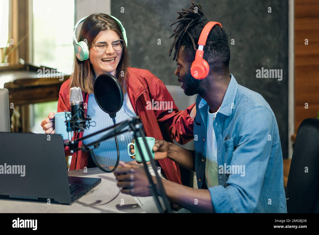 Deux créateurs de contenu sont assis à une table pour enregistrer un podcast. L'homme afro-américain et la femme caucasienne portent des écouteurs et se concentrent sur une tablette Banque D'Images