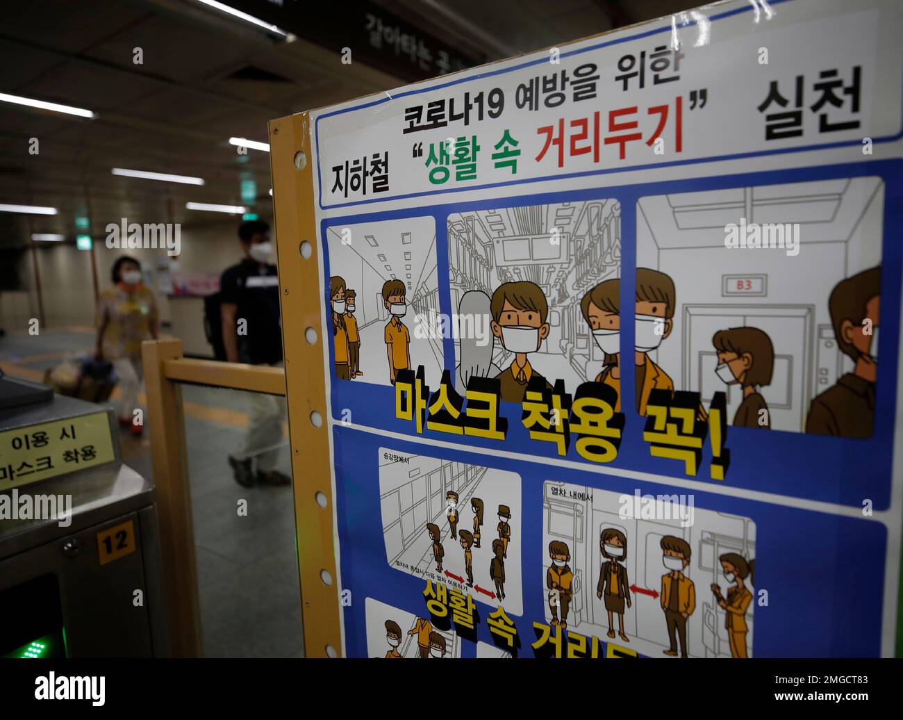 Passengers wearing face masks walk near a banner displaying precautions against the coronavirus at the subway station in Seoul, South Korea, Sunday, June 28, 2020. The letters read "Wear a mask and social distance." (AP Photo/Lee Jin-man) Banque D'Images