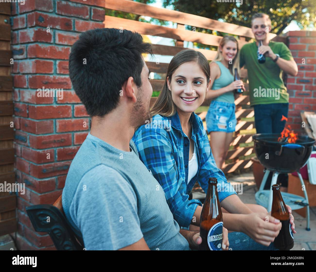 Amis (pour le moment). un jeune homme et une jeune femme bavardant et prenant des bières au barbecue avec des amis. Banque D'Images