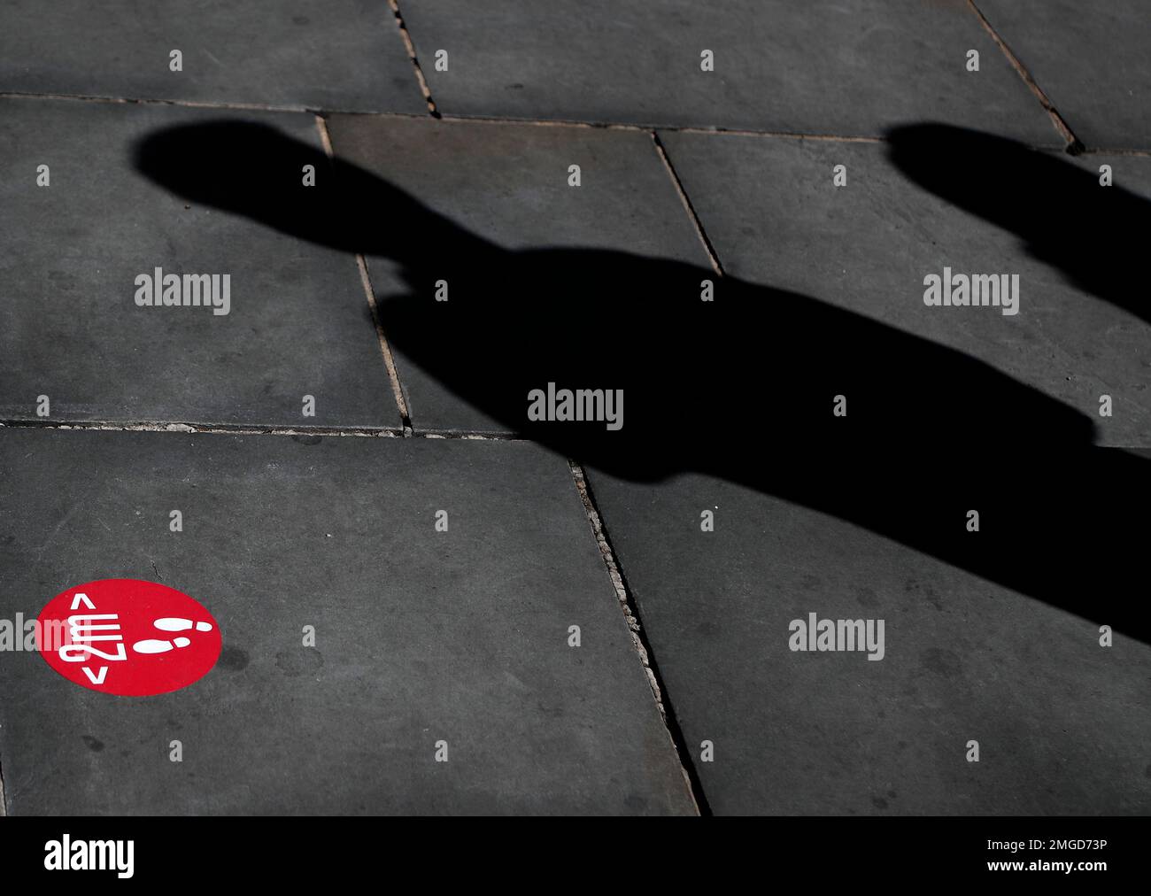 Two people cast a shadow as they queue beside a two meter distance sign at a shop in London, Monday, June 22, 2020. The two-metre social distancing rule will be under review as the UK relax coronavirus lockdown measures implemented to stem the spread of the virus. (AP Photo/Frank Augstein) Banque D'Images