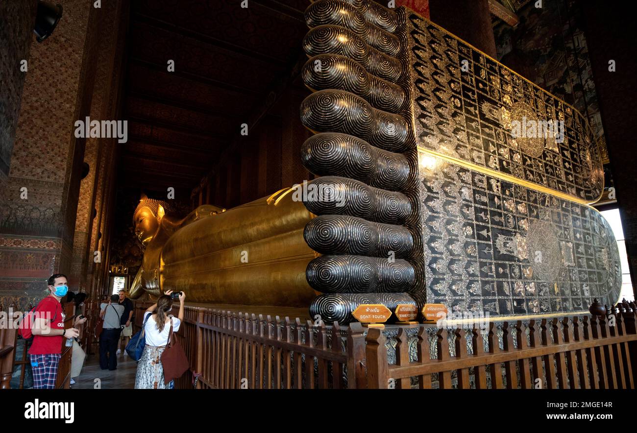 In this Friday, March 13, 2020, photo, tourists take a photograph with the statue of a giant Buddha at Wat Pho in Bangkok, Thailand. Wat Pho, which is one of Thailand's major tourist attractions and famous for housing the golden 46-meter-long (151-foot-long) Reclining Buddha, has barred entry to foreigners, professing fear that they could spread COVID-19. (AP Photo/Sakchai Lalit) Banque D'Images