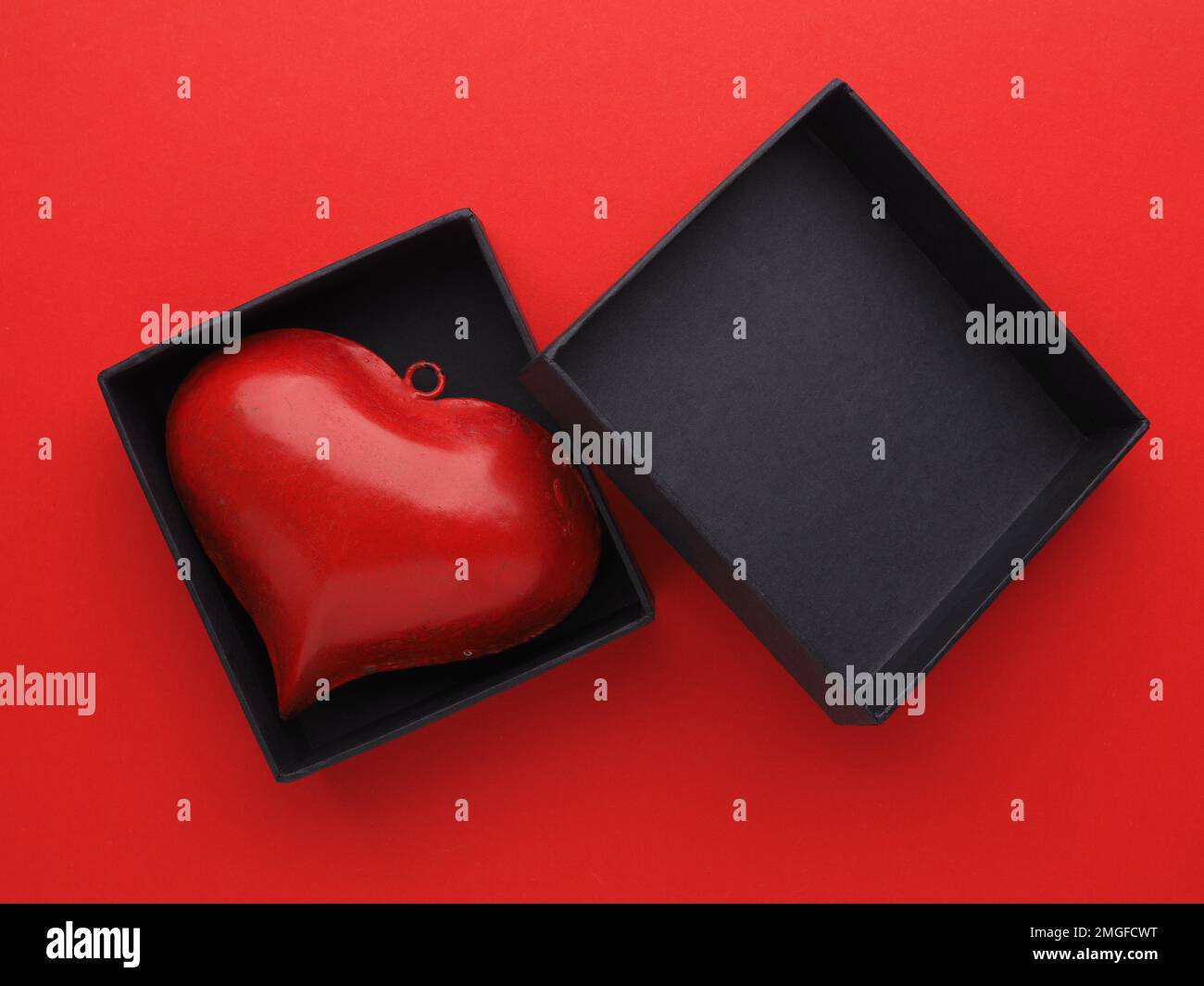 Cœur métallique rouge dans une boîte cadeau noire sur fond rouge, concept de Saint-Valentin ou d'anniversaire Banque D'Images