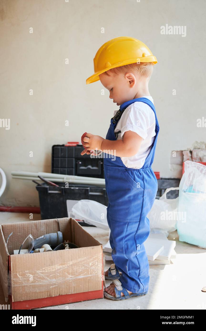 Petit garçon près d'une boîte en carton avec des outils et des matériaux pour la rénovation de la maison. Enfant ouvrier de construction tenant un composant de construction. Banque D'Images