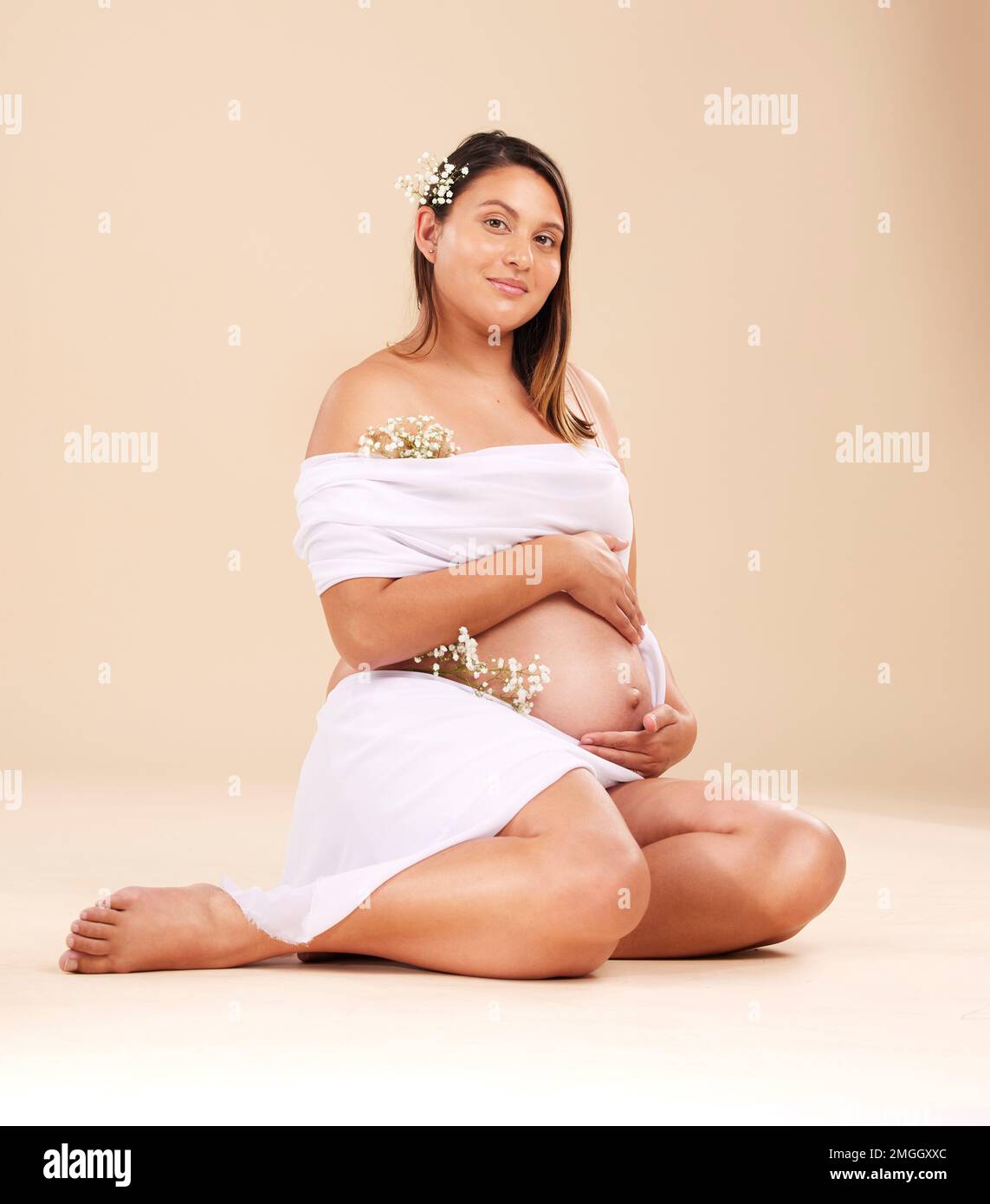 Grossesse, beauté et portrait d'une femme en studio avec du matériel de mousseline et des fleurs tenant son estomac. Maternité, santé prénatale et grossesse Banque D'Images