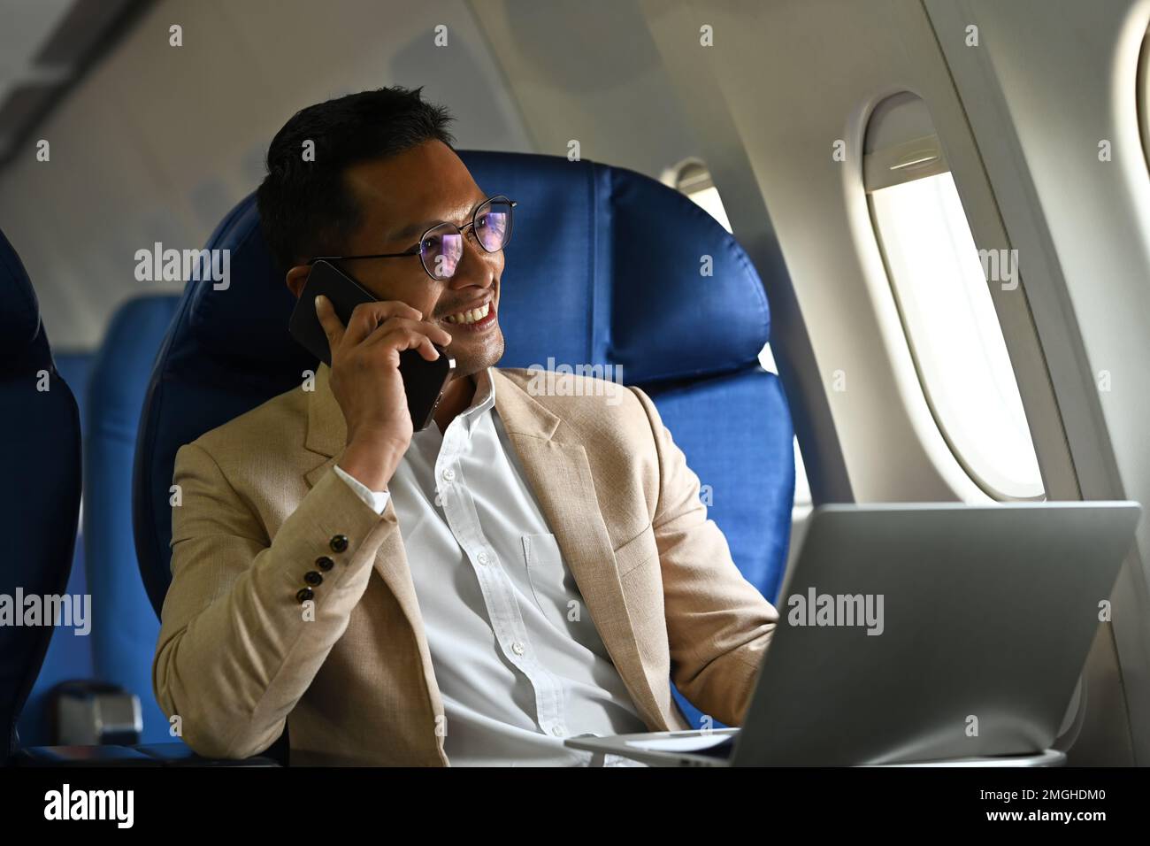 Un homme d'affaires qui a réussi à parler sur un téléphone portable tout en étant assis dans la cabine d'avion près des fenêtres Banque D'Images