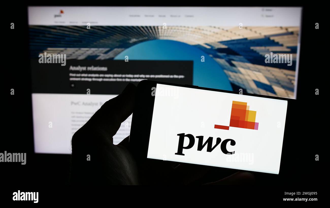 Personne tenant un smartphone avec le logo de la société de conseil PricewaterhouseCoopers (PWC) à l'écran devant le site Web. Mise au point sur l'affichage du téléphone. Banque D'Images