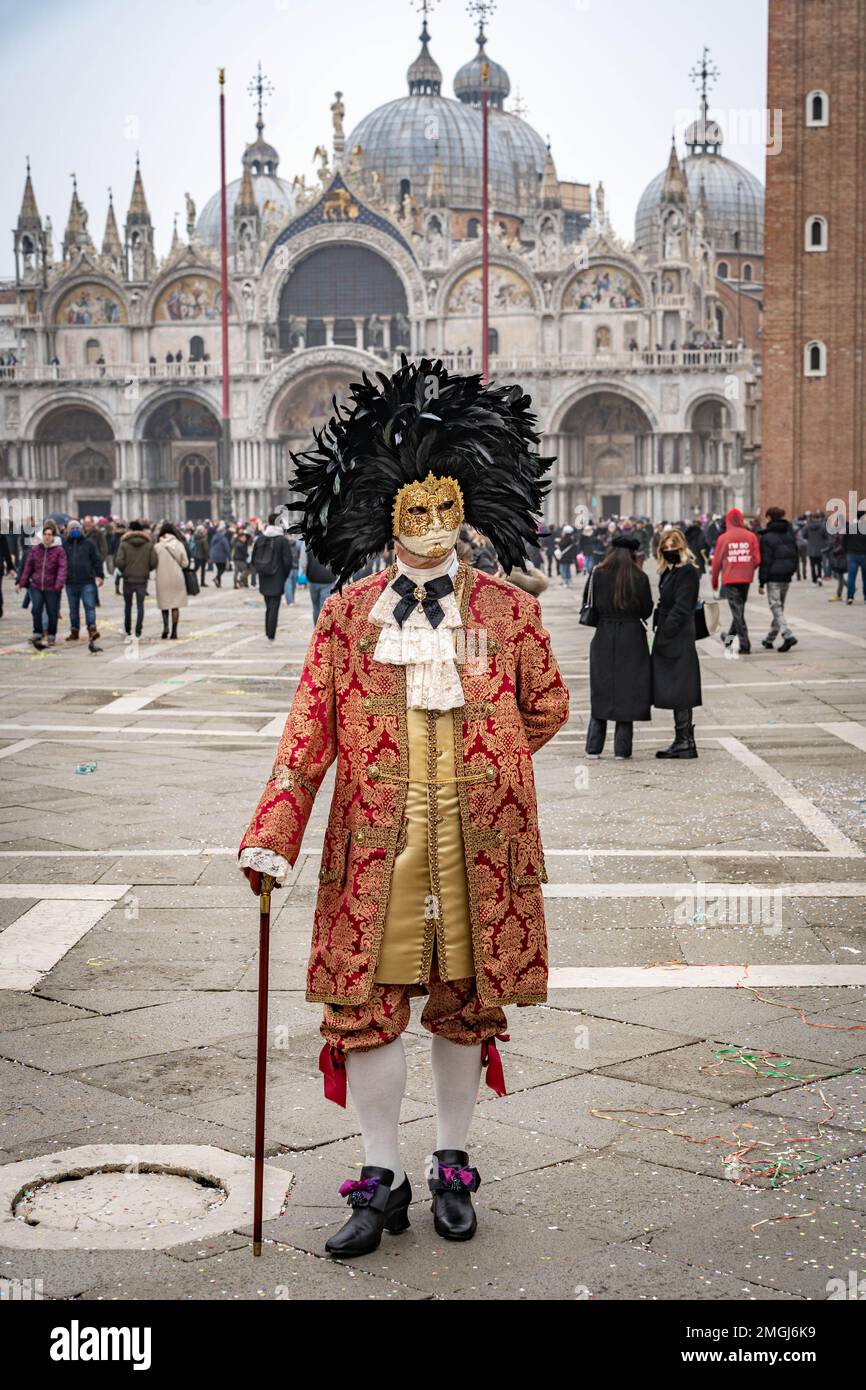 Un homme d'âge moyen en costume rouge vintage avec col en dentelle, portant un masque de carnaval bordé d'un cercle de plumes noires élevées, est seul avec Banque D'Images