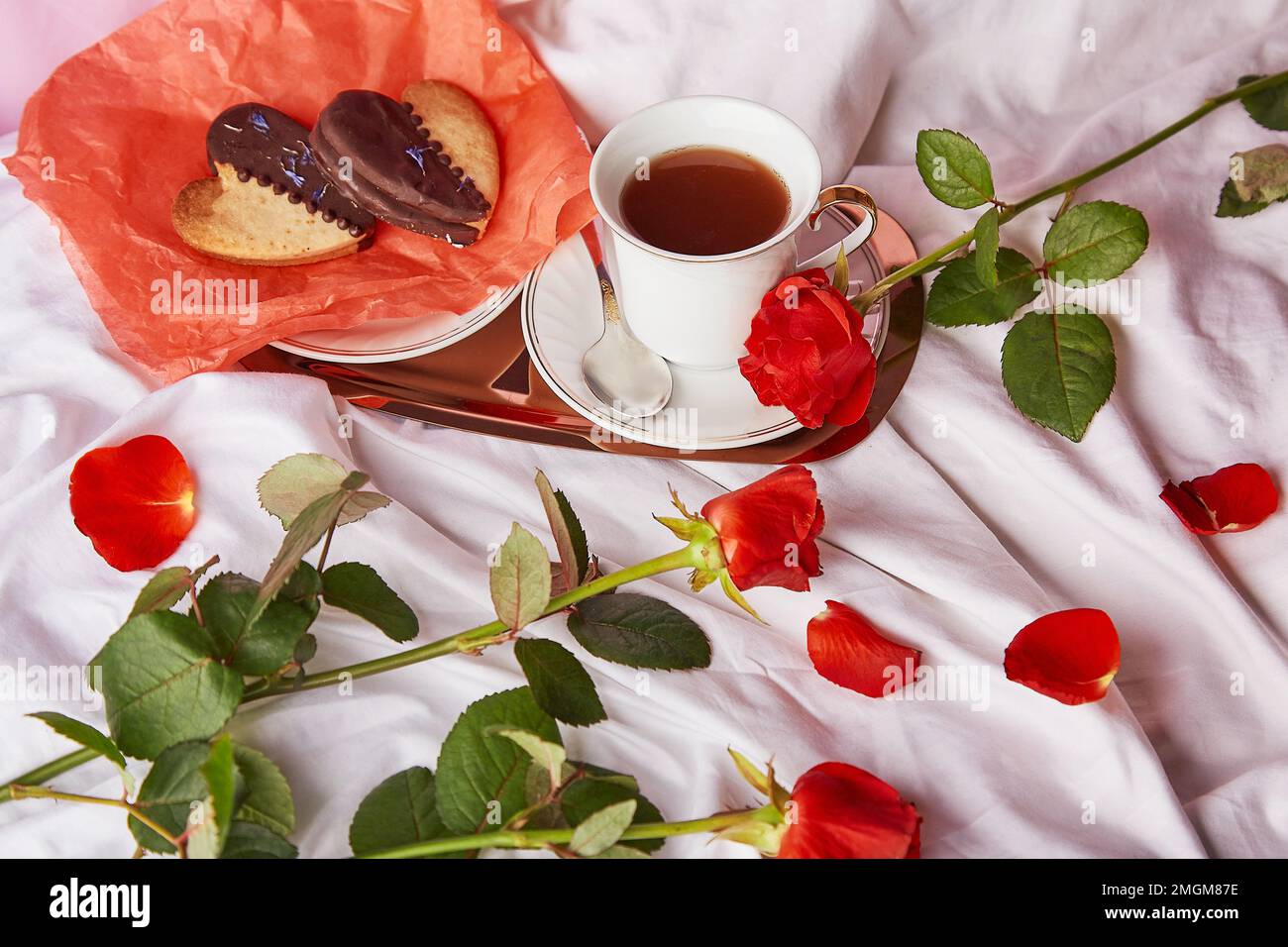 St Valentines petit déjeuner au lit parmi les roses traditionnelles rouges - biscuits en forme de coeur vegan et tasse de café sur les draps. Esthétique, vacances romantique au lagon. Banque D'Images