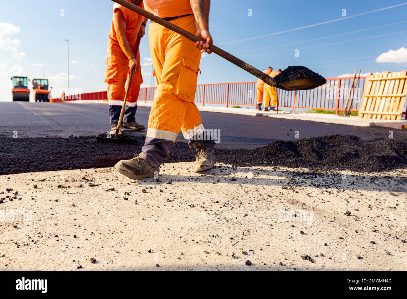 Peu de travailleurs utilisent des pelles pour niveler, mettre en place une couche de tarmac frais à la bonne mesure, verser de l'asphalte chaud. Banque D'Images