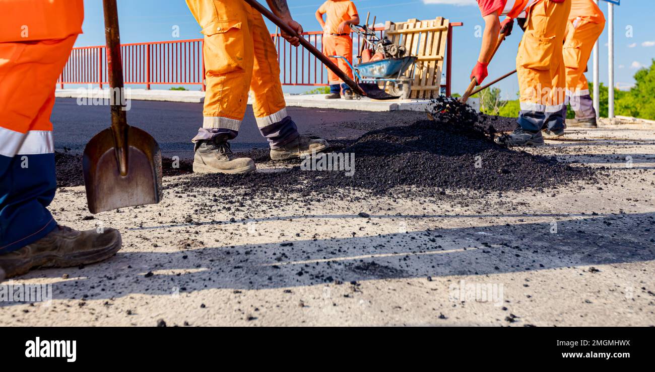 Peu de travailleurs utilisent des pelles pour niveler, mettre en place une couche de tarmac frais à la bonne mesure, verser de l'asphalte chaud. Banque D'Images