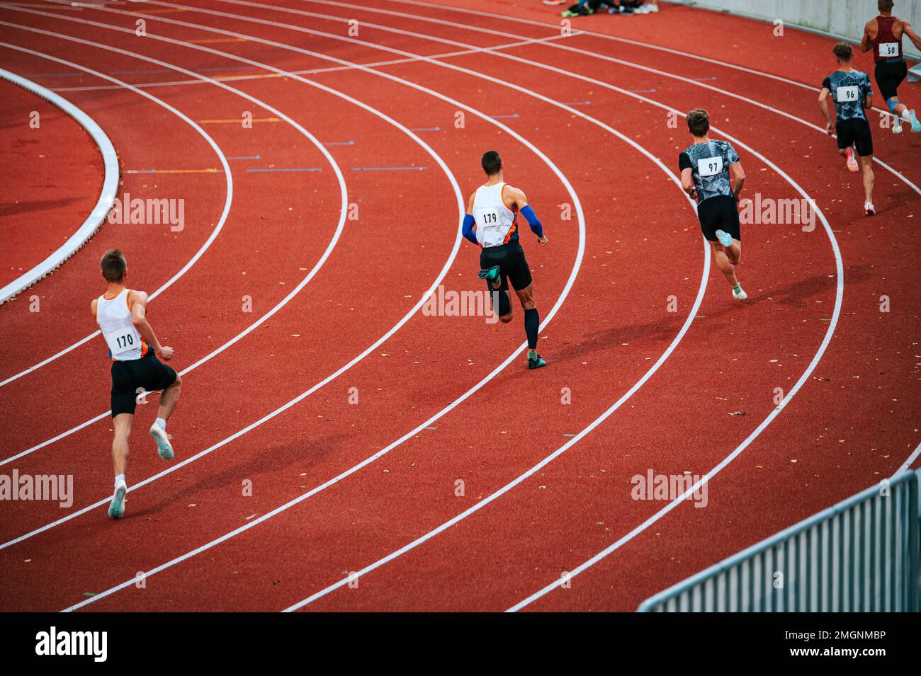 Groupe d'athlètes masculins déterminés prêts à décoller au début d'une course de 400m sur la piste. Parfait pour promouvoir la persévérance, l'athlétisme et la physique Banque D'Images