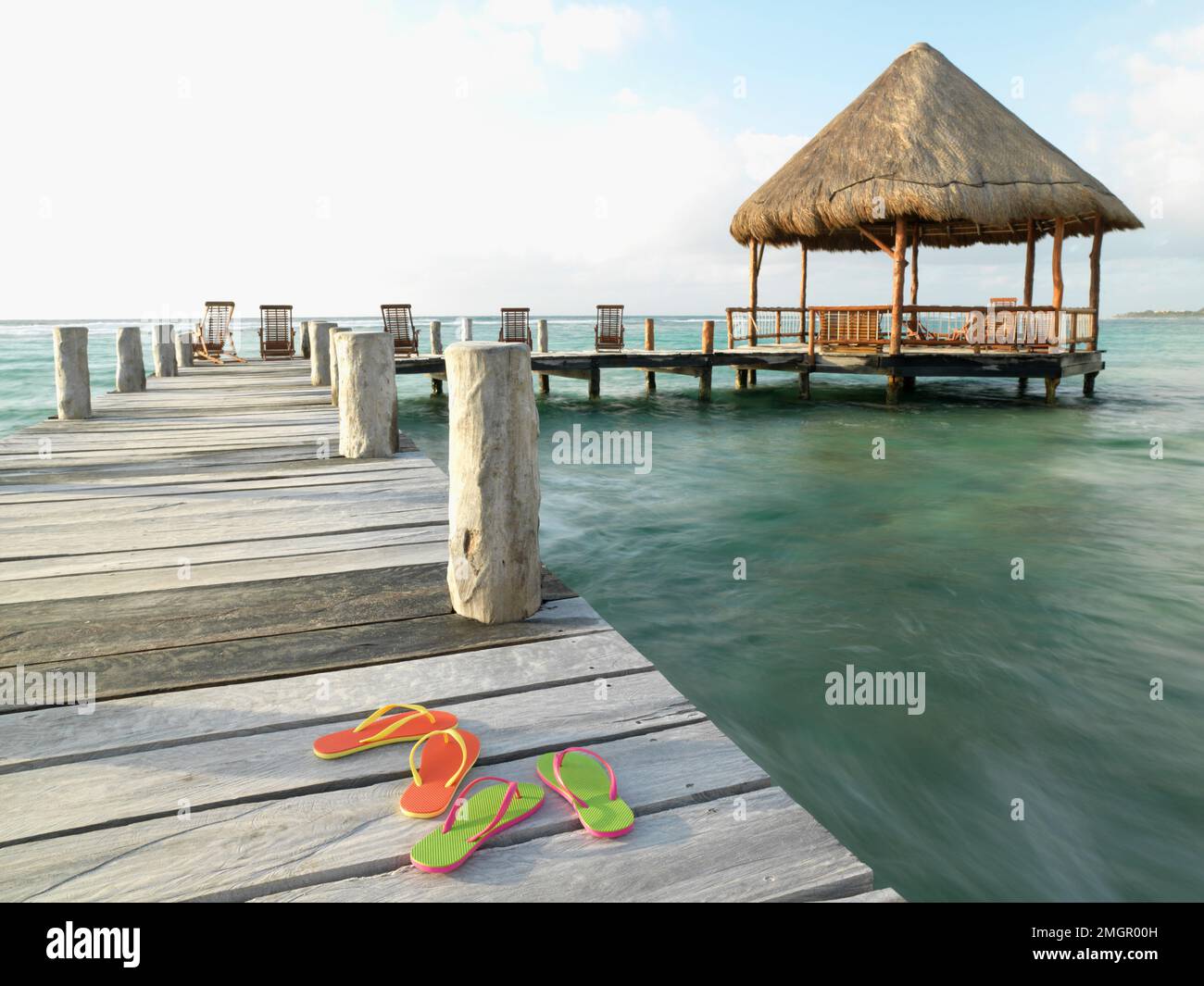 Mexique, Akumal, sandales à bascule sur une jetée avec une palapa dans le fond Banque D'Images