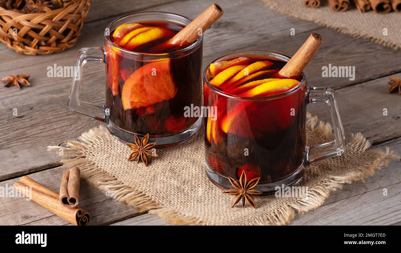 Vin chaud dans des mugs en verre avec des épices et des agrumes sur une vieille table en bois Banque D'Images