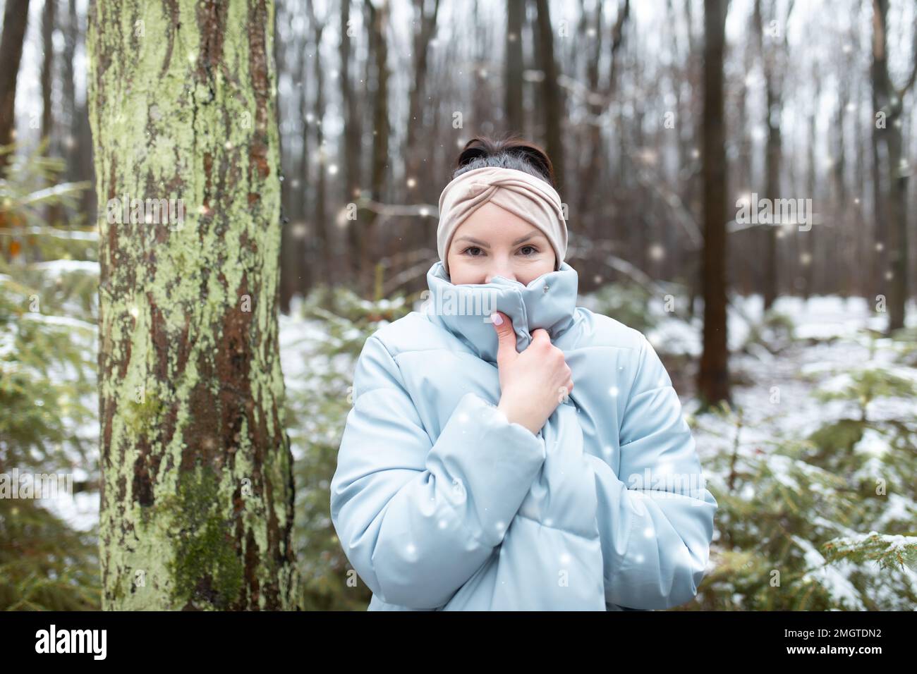Femme heureuse en forêt d'hiver. Portrait de femme dans un parc à neige. Femme adulte avec serre-tête cache le visage sous la veste. Banque D'Images