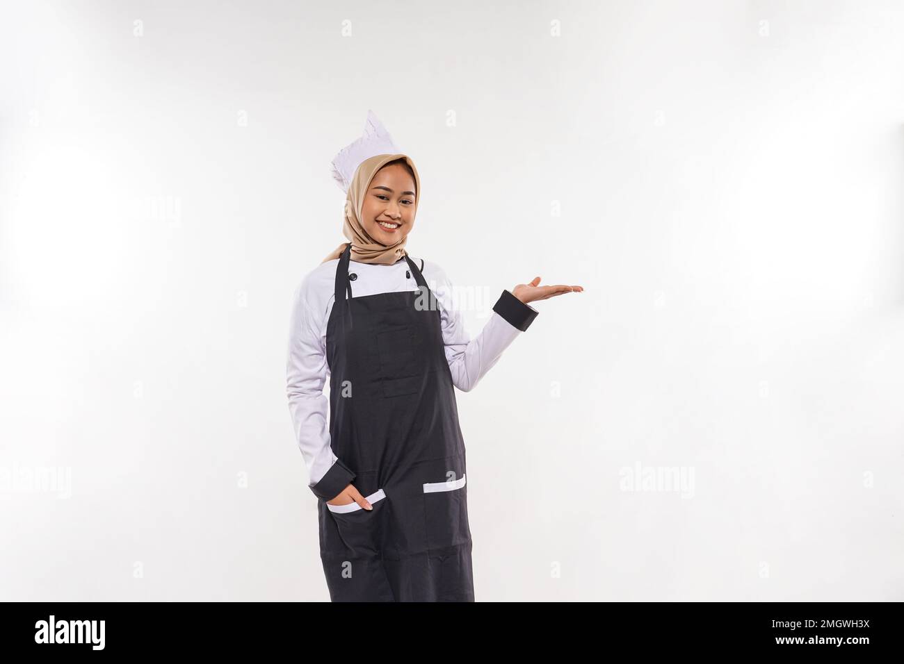 une belle cuisinière avec hijab pointant sur son côté gauche Banque D'Images